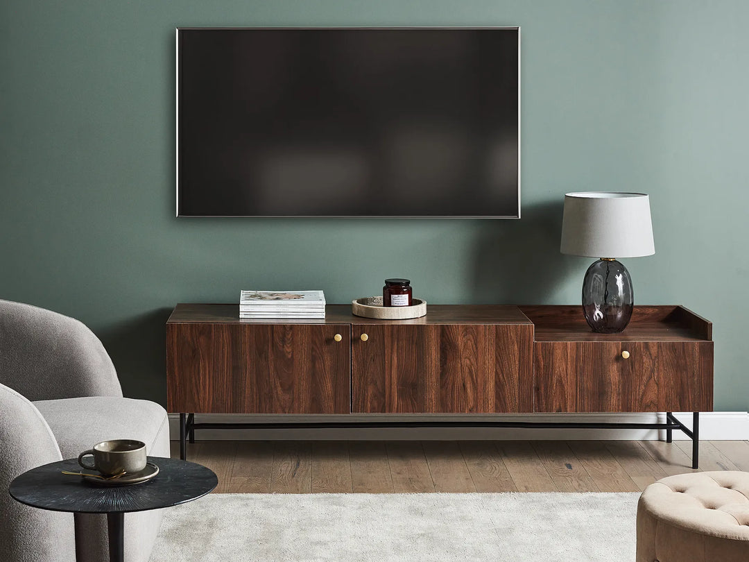 Modern living room with a wooden console table, gray armchair, and television mounted on a green wall.