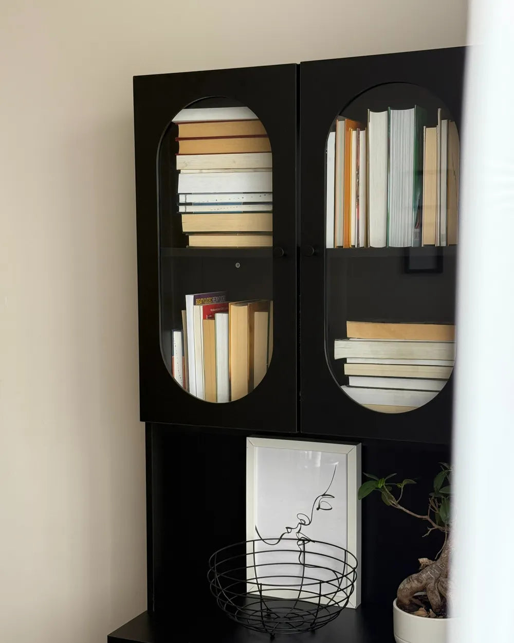 Black bookshelf with books and decorative items against a beige wall
