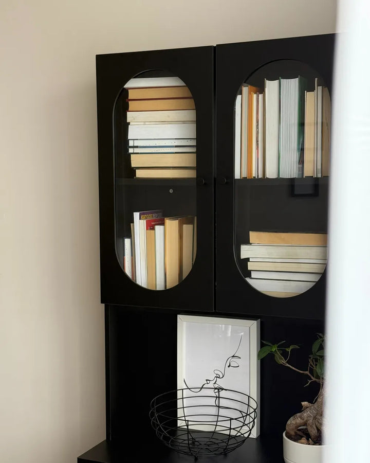 Black bookshelf with books and decorative items against a beige wall