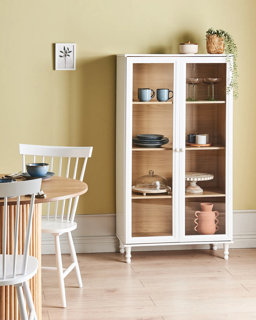 White display cabinet with glass doors in a room with a table and chairs.