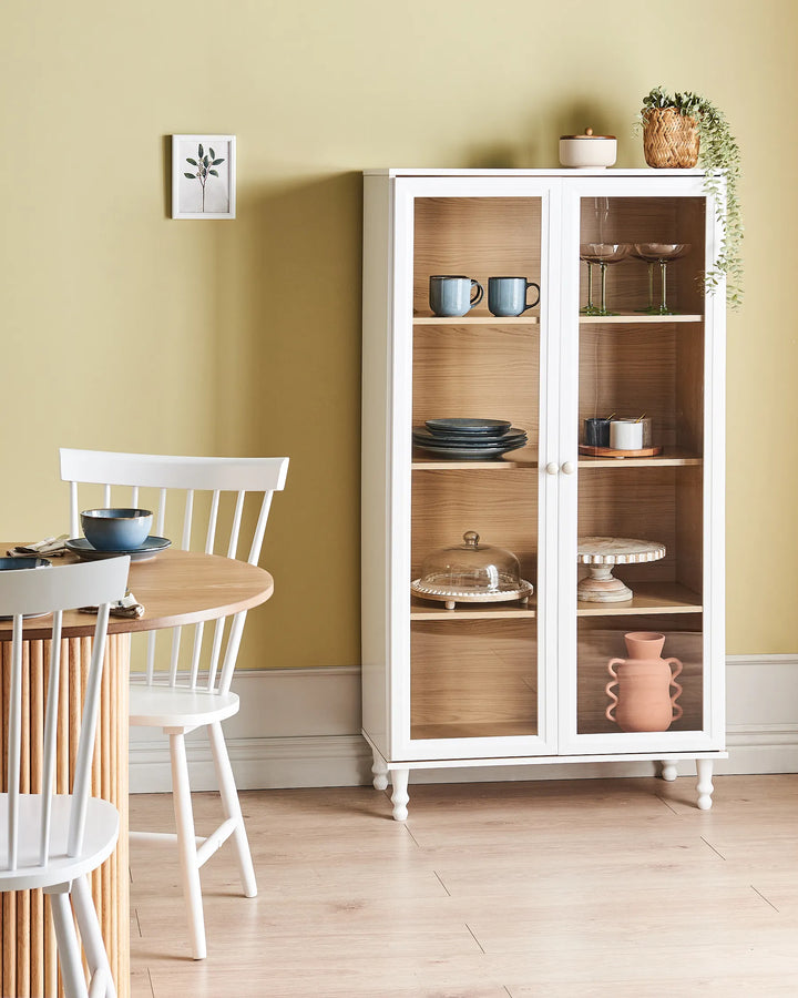 White display cabinet with glass doors in a room with a table and chairs.