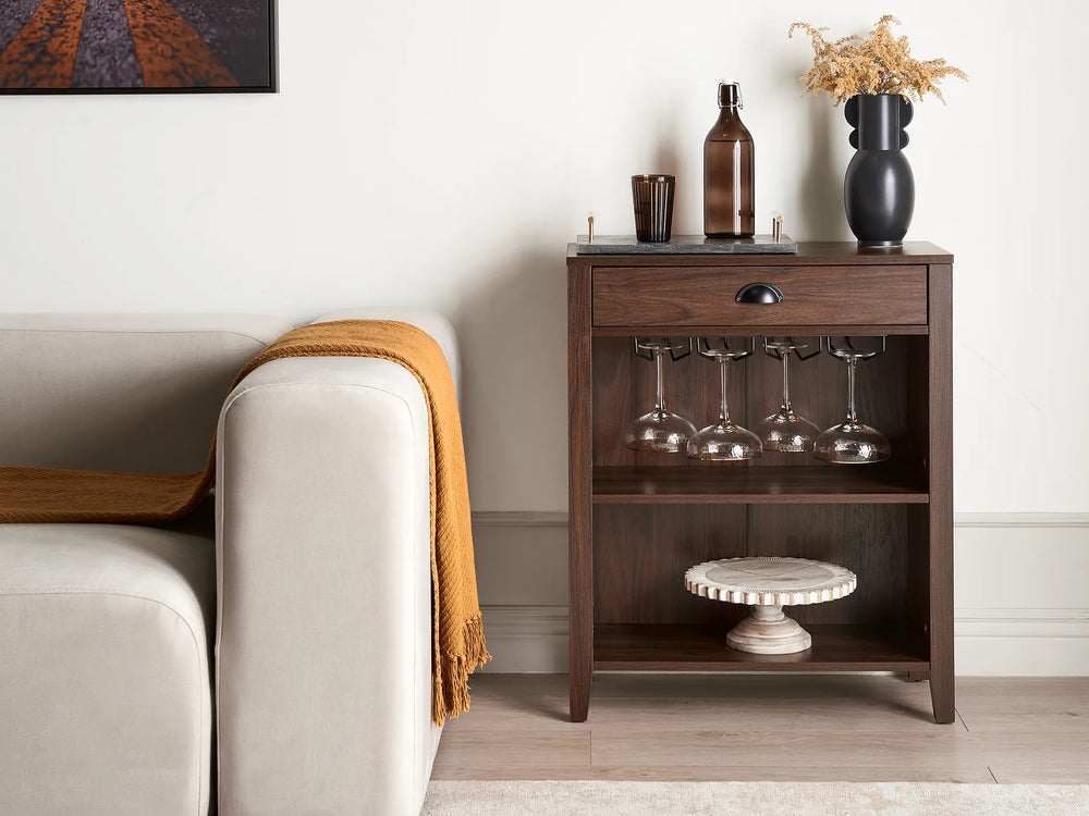 Wooden sideboard with wine glasses and bottles next to a beige sofa.
