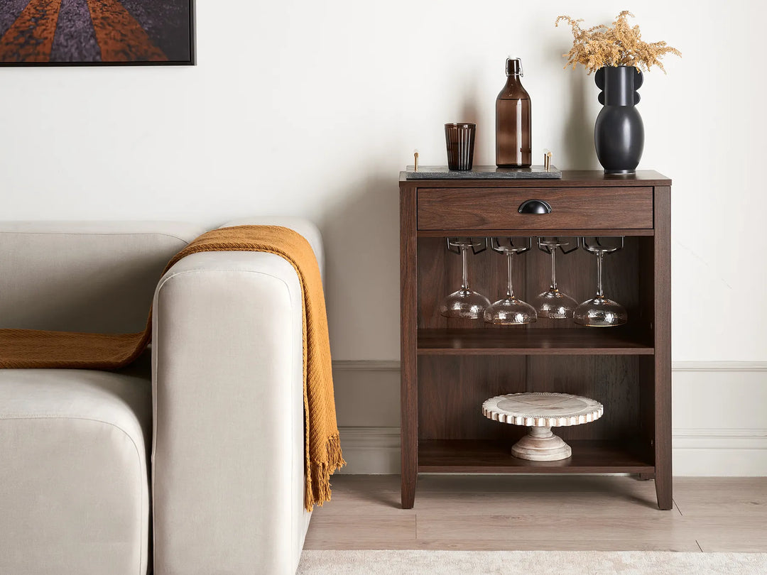 Wooden sideboard with wine glasses and bottles next to a beige sofa.
