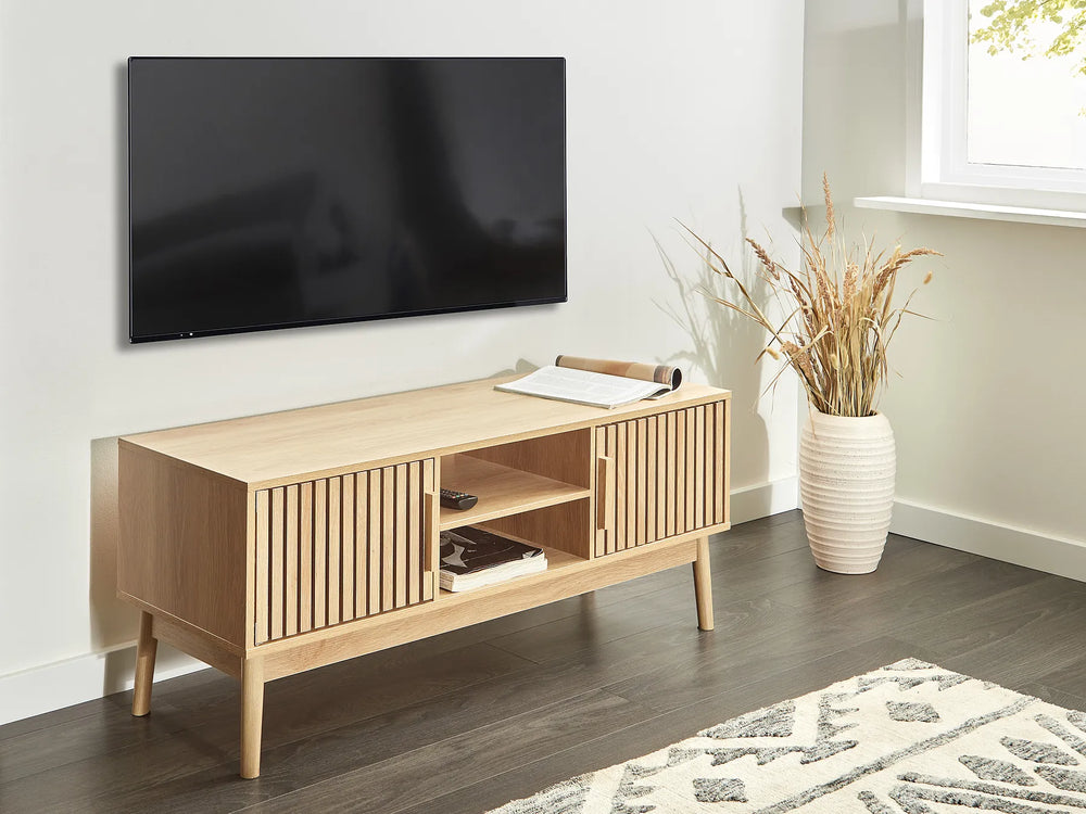 Wooden TV stand with a television mounted on the wall in a room with a rug and plant.