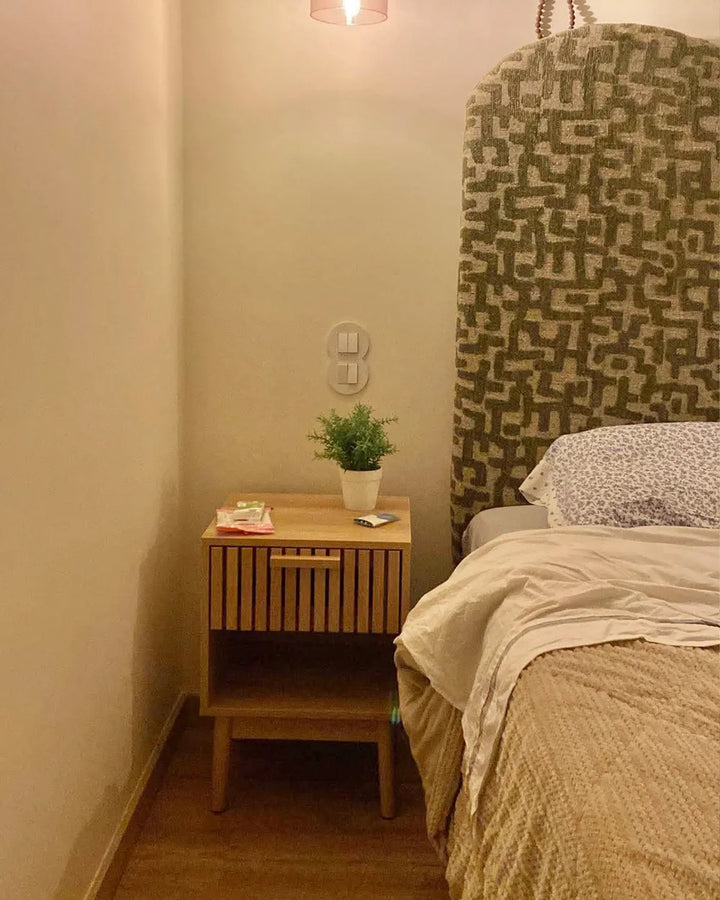 Bedroom with wooden nightstand, plant, and patterned headboard.