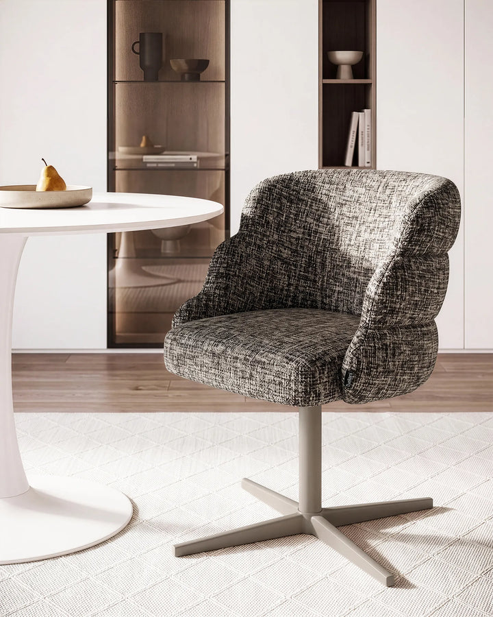 A modern upholstered swivel chair with a textured gray and white woven fabric, set in a bright, contemporary dining room next to a white table.
