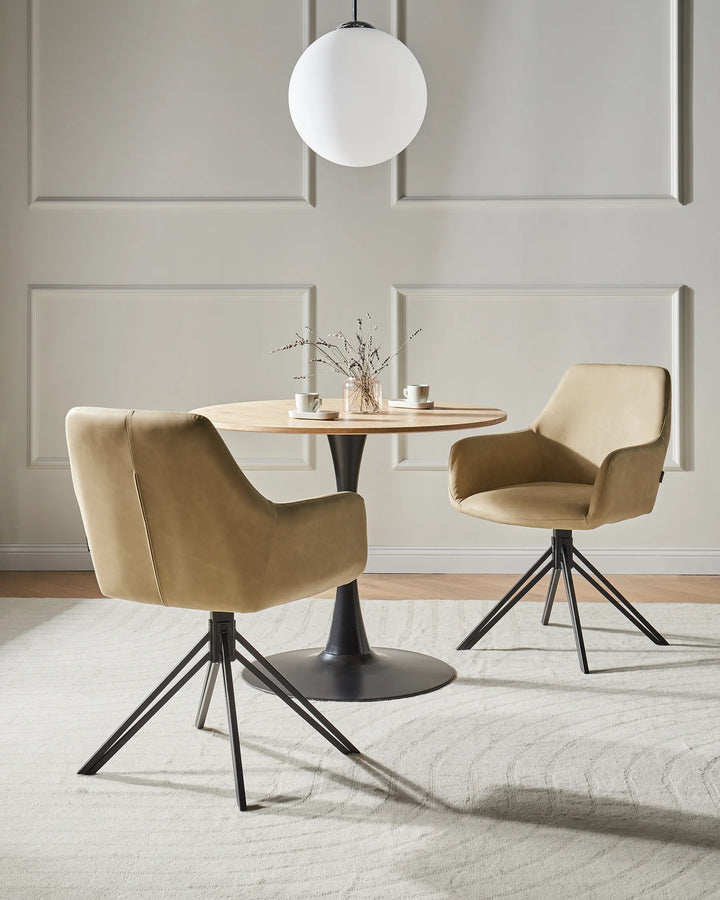 Two modern beige upholstered dining chairs with black metal swivel bases arranged around a round wooden table in a bright, neutral dining room.