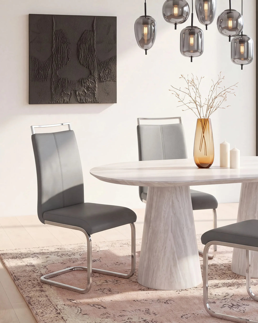 A modern dining room scene featuring a round white marble-look table with a white faux-leather upholstered chair and a gray upholstered chair with a chrome cantilever base, styled with a glass vase and candles.