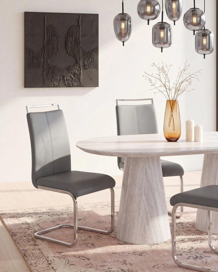 A modern dining room scene featuring a round white marble-look table with a white faux-leather upholstered chair and a gray upholstered chair with a chrome cantilever base, styled with a glass vase and candles.