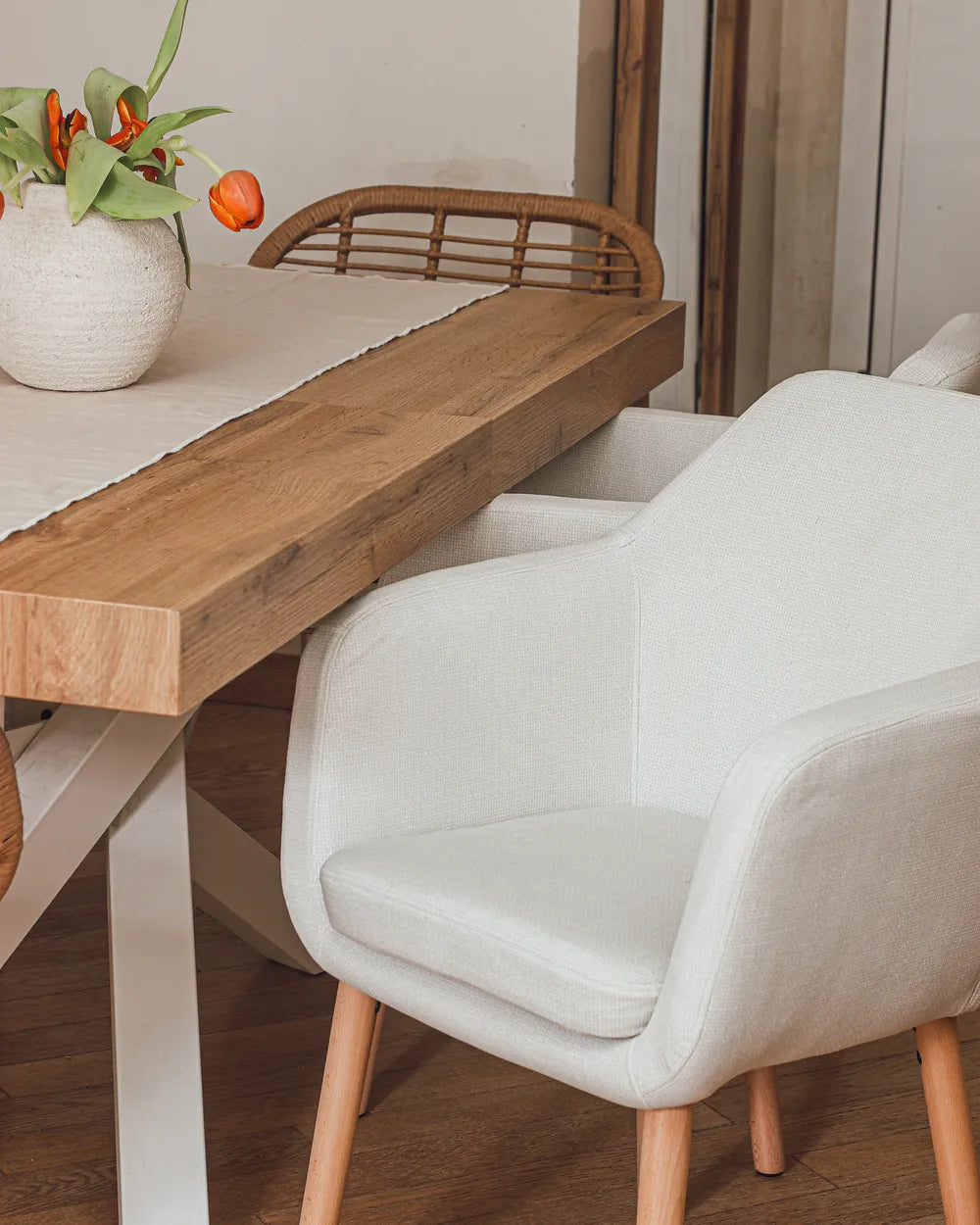 Dining table with a white chair and a vase of flowers on a wooden floor.