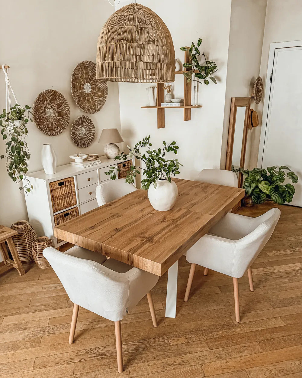 Dining room with wooden table and white chairs, decorative wall art, and plants.