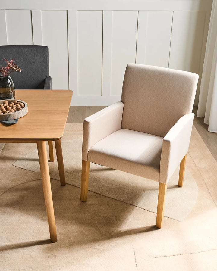 Beige chair next to a wooden table in a room with light-colored walls and flooring.