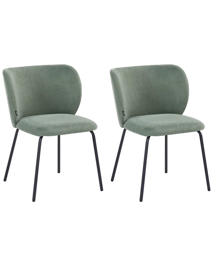 Two matching upholstered dining chairs in a muted sage green velvet fabric with slim black metal legs, shown side by side on a plain white background.