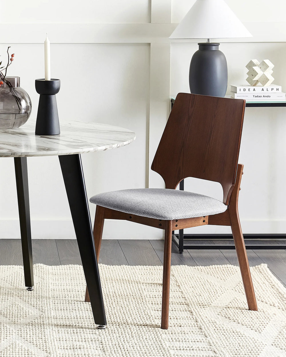 Dining chair with wooden frame and gray cushion next to a round table in a modern interior setting.