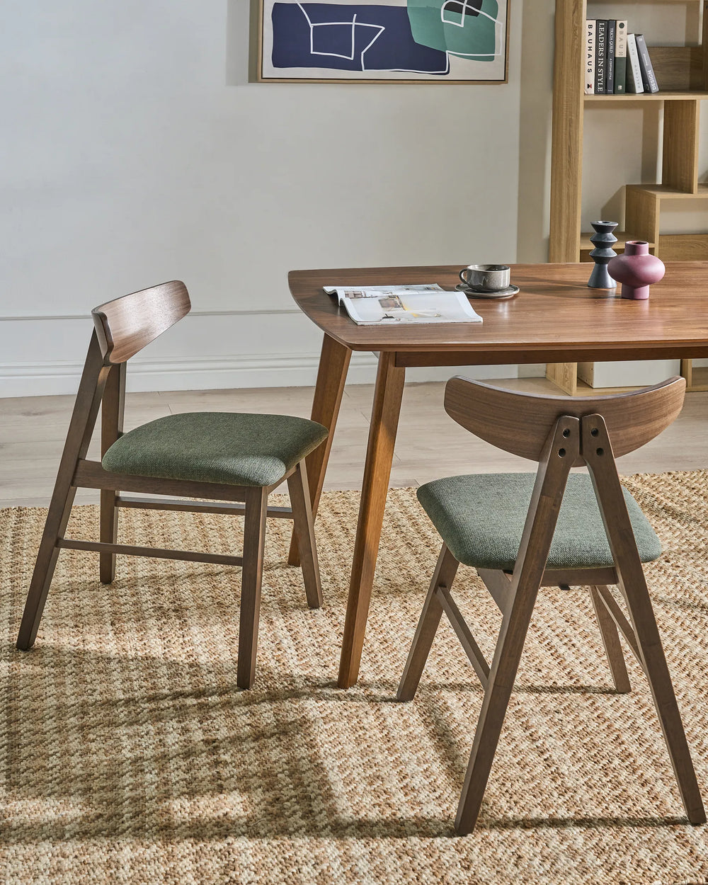 Wooden dining table with two chairs in a room with a rug and wall art.