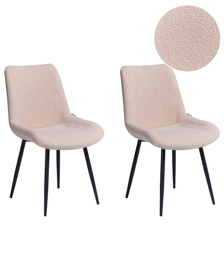 Two upholstered dining chairs in a light blush pink bouclé fabric with black tapered legs, shown on a white background with a circular fabric close-up inset.