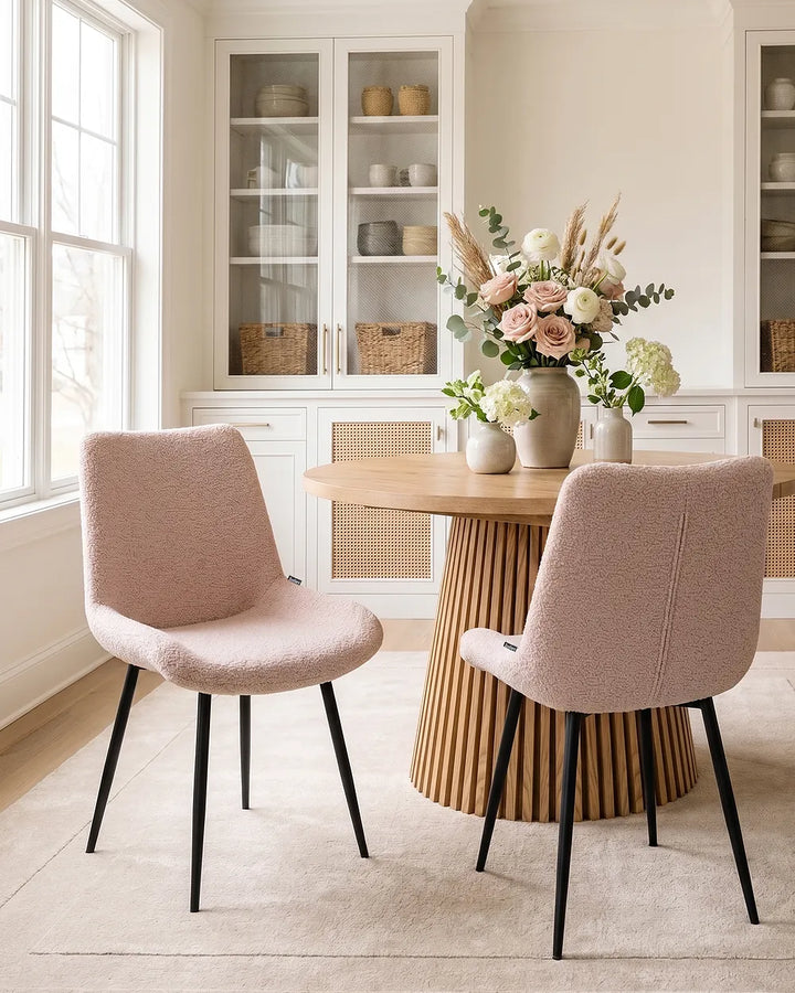 Two upholstered dining chairs in a light blush pink bouclé fabric with black tapered legs