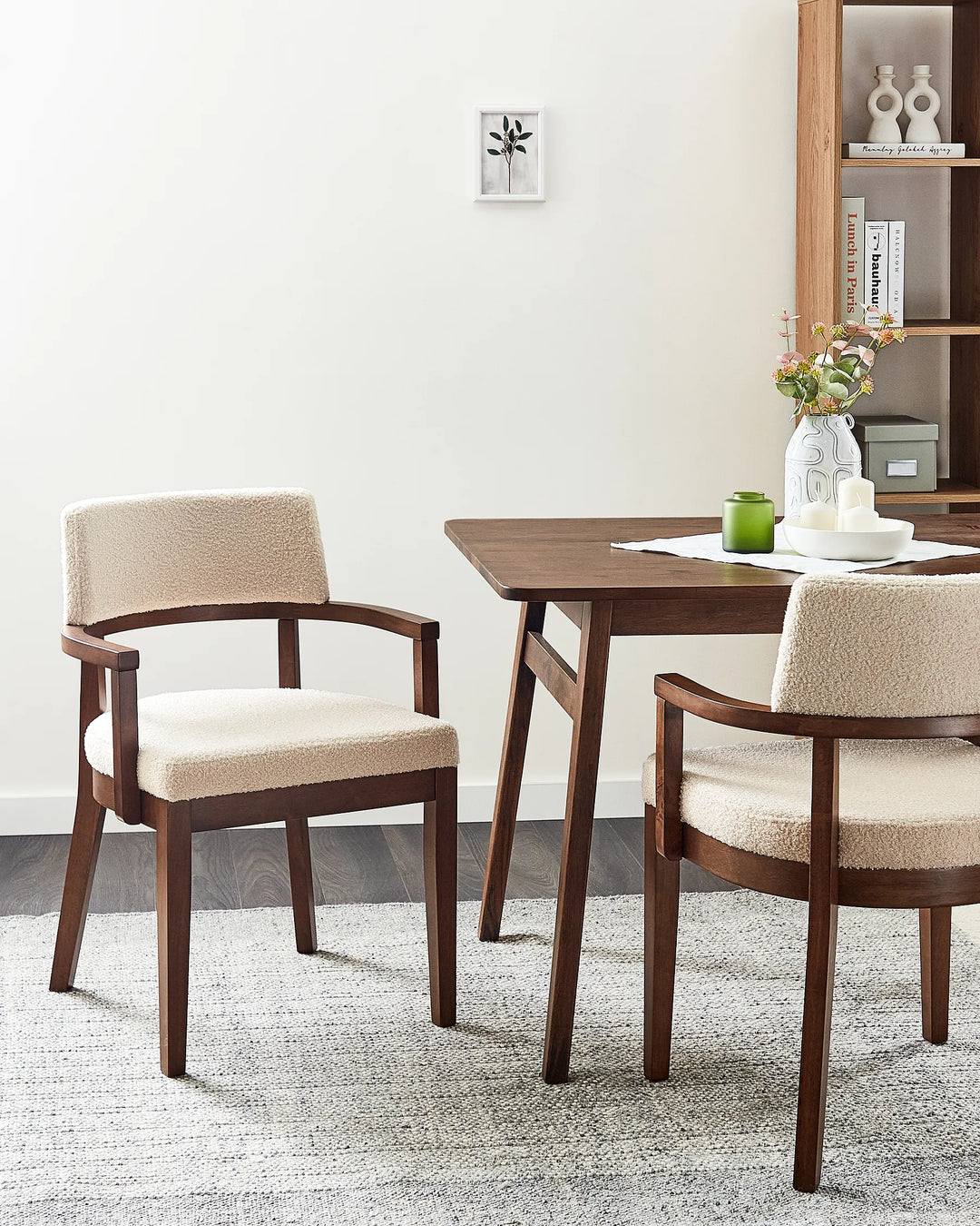 Two mid-century modern dining chairs with textured cream bouclé upholstery and dark brown wooden frames, shown in a styled dining room setting next to a wooden table.