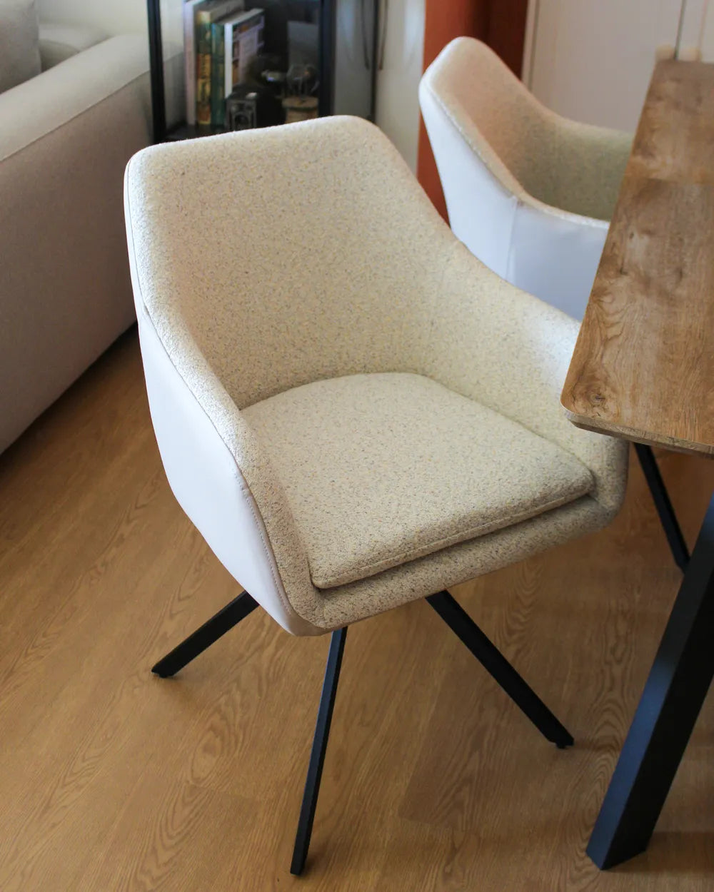 Beige chair with black legs on a wooden floor next to a table.