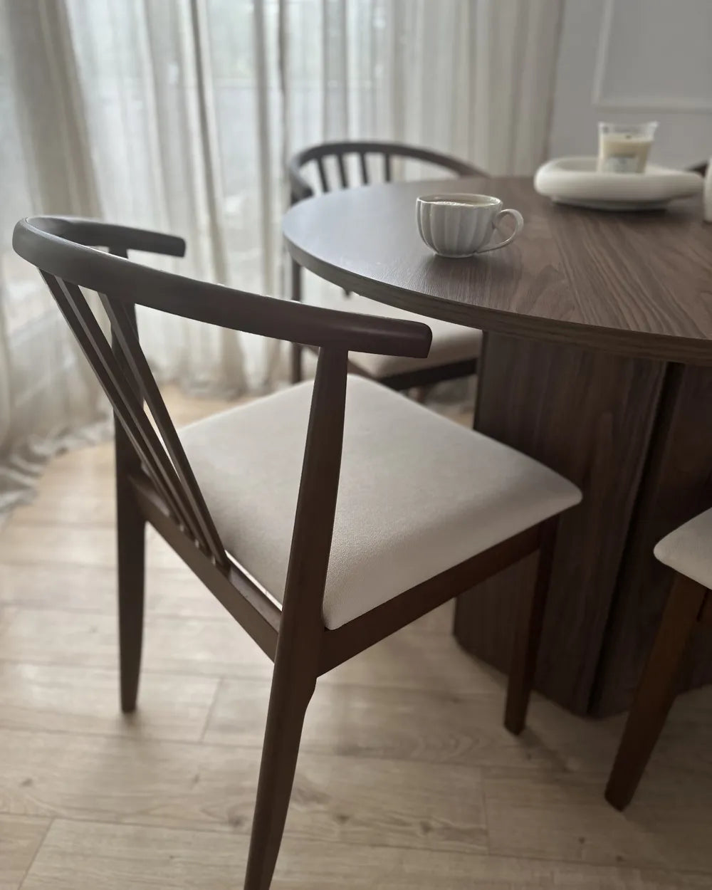 Dining room with wooden table and chairs, light curtains in the background