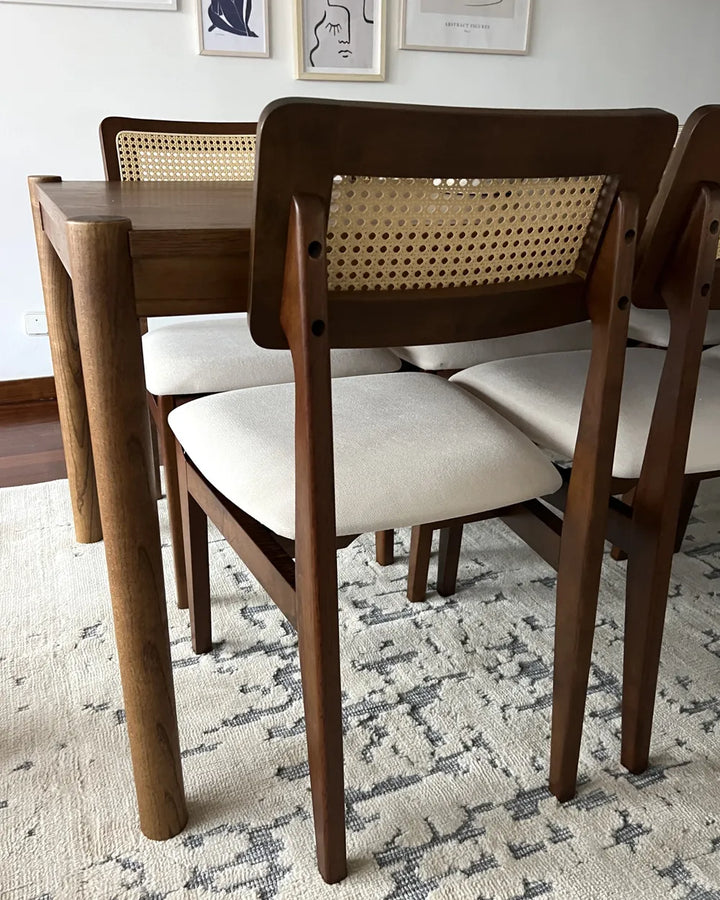 Dining table set with wooden chairs and cane backrests on a patterned rug.