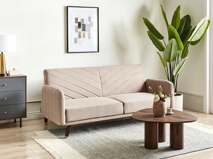 Beige sofa in a living room with a coffee table, plant, and wall art.