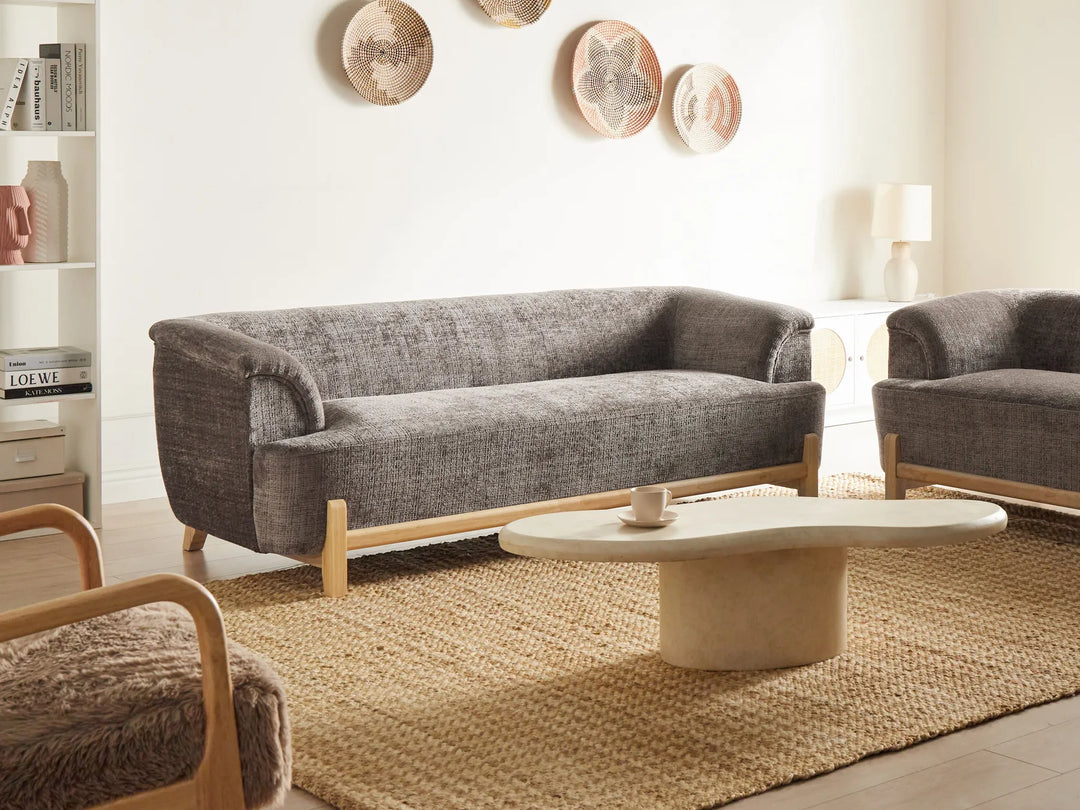 Modern living room with gray sofa, wooden armchair, and round coffee table.