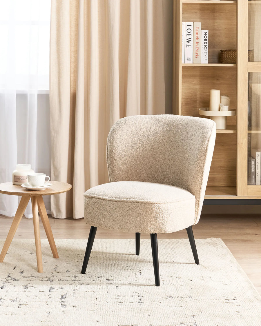 Beige armchair in a room with a wooden side table and bookshelf.