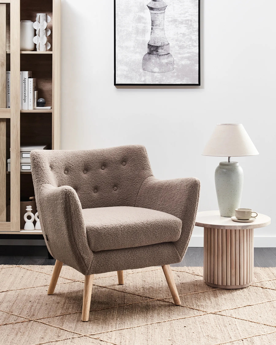 Beige armchair in a living room setting with a side table and lamp.