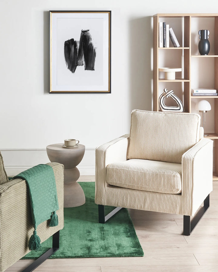 Beige armchair in a living room with a green rug and bookshelf.