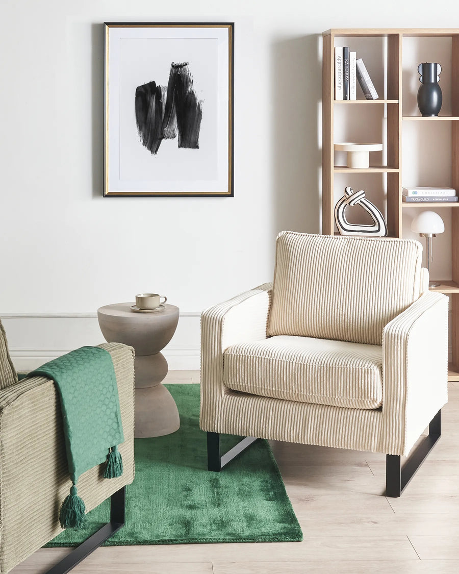 Beige armchair in a living room with a green rug and bookshelf.