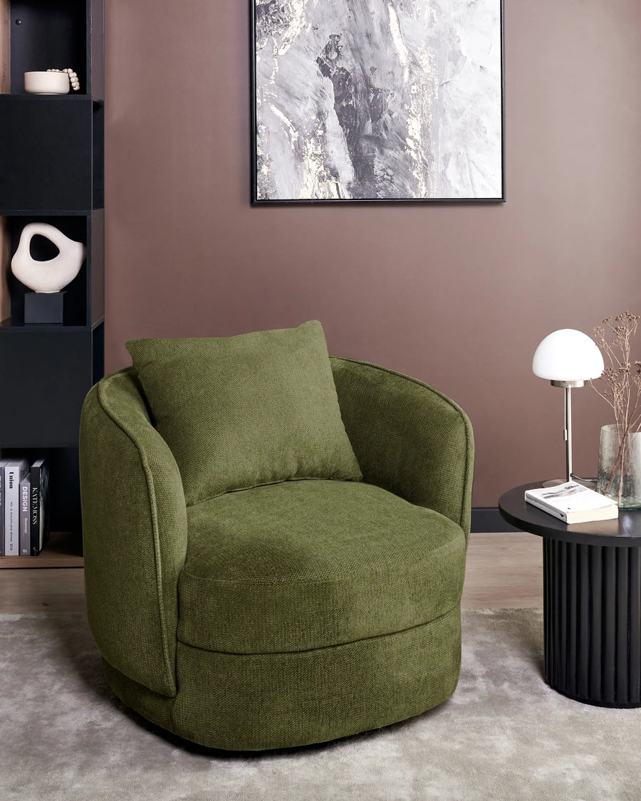 Green armchair in a modern living room with a bookshelf and abstract painting.