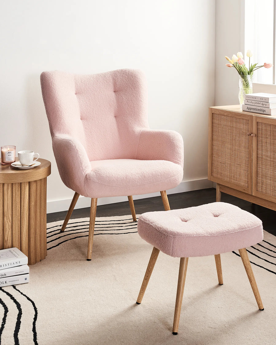 Pink armchair and ottoman with wooden side table and cabinet in a room.
