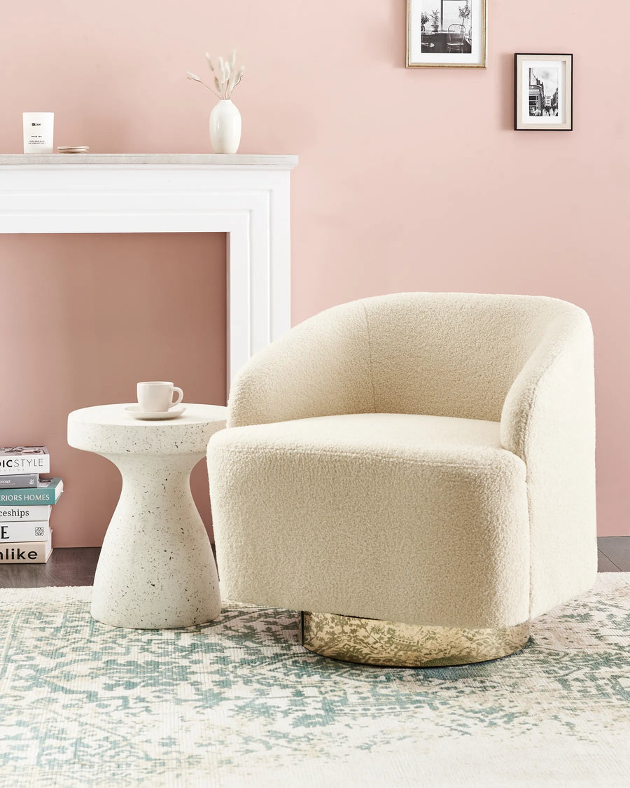 Beige armchair in a living room with a pink wall, white fireplace, and small table.