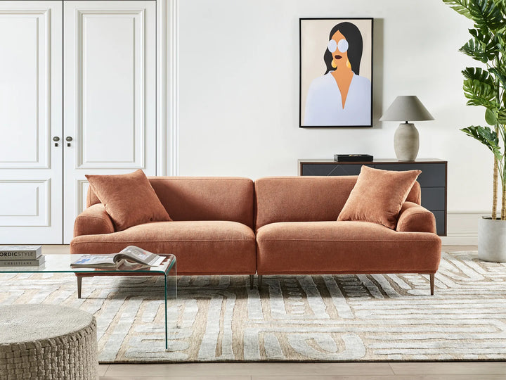 Coral sofa in a living room with a glass coffee table, rug, and wall art.