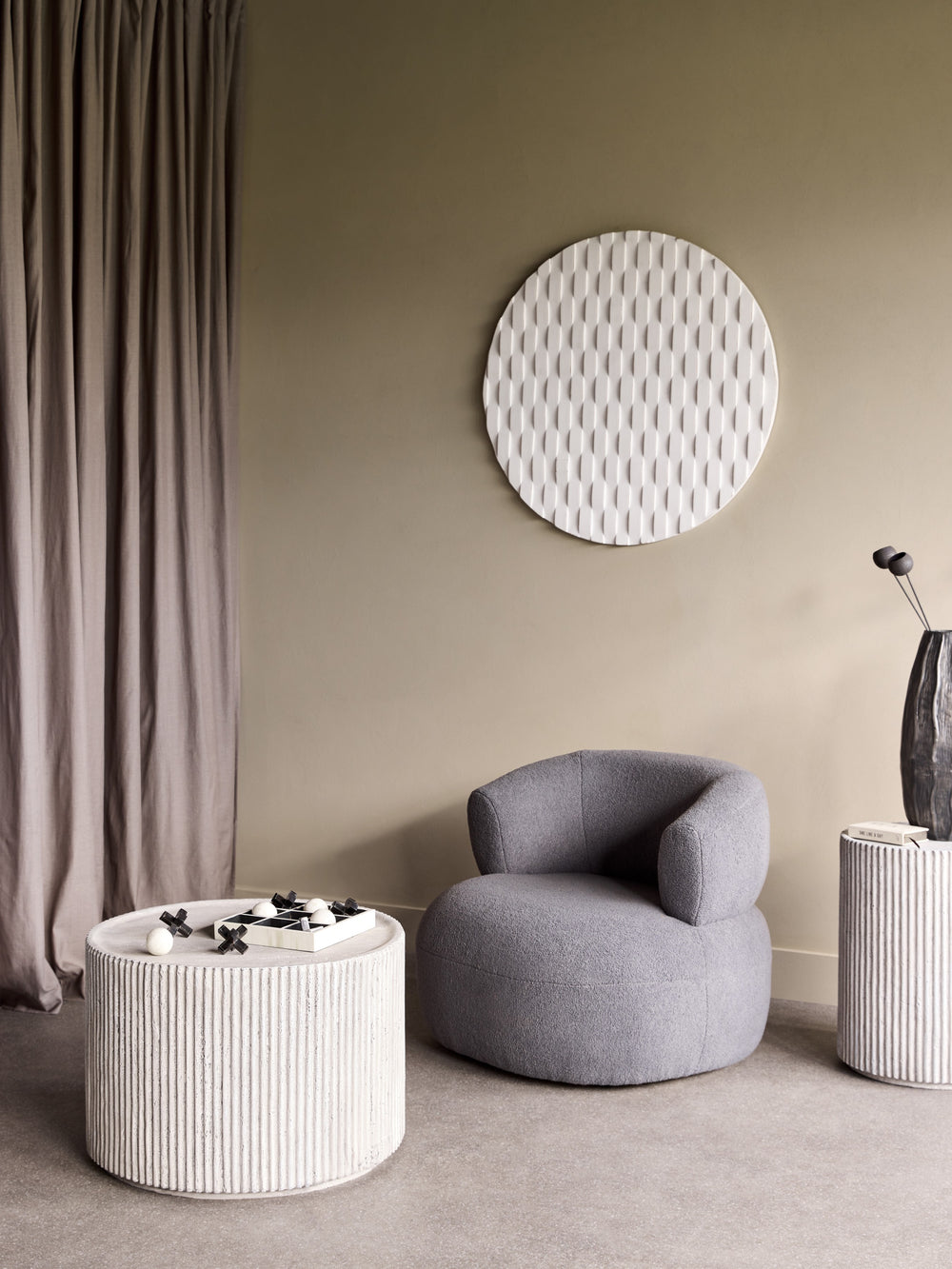 Modern interior with a gray chair, round ottoman, and decorative wall piece.
