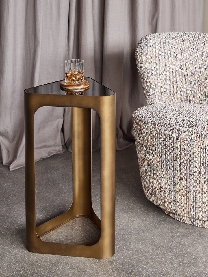 Bronze side table with a glass of whiskey next to a textured armchair.