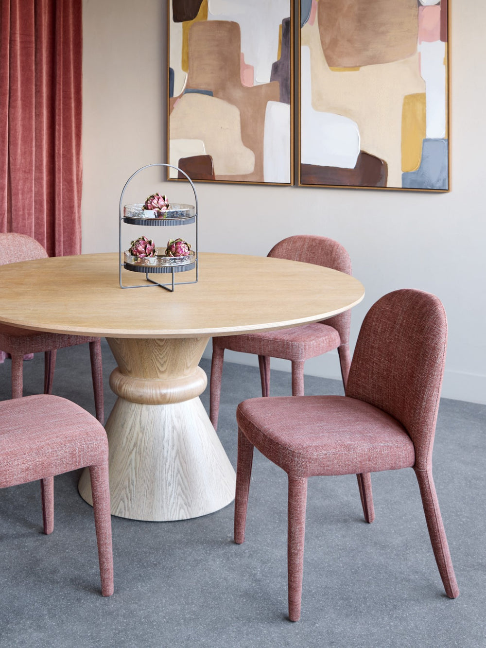Dining room with a round wooden table and pink chairs, abstract art on the wall.
