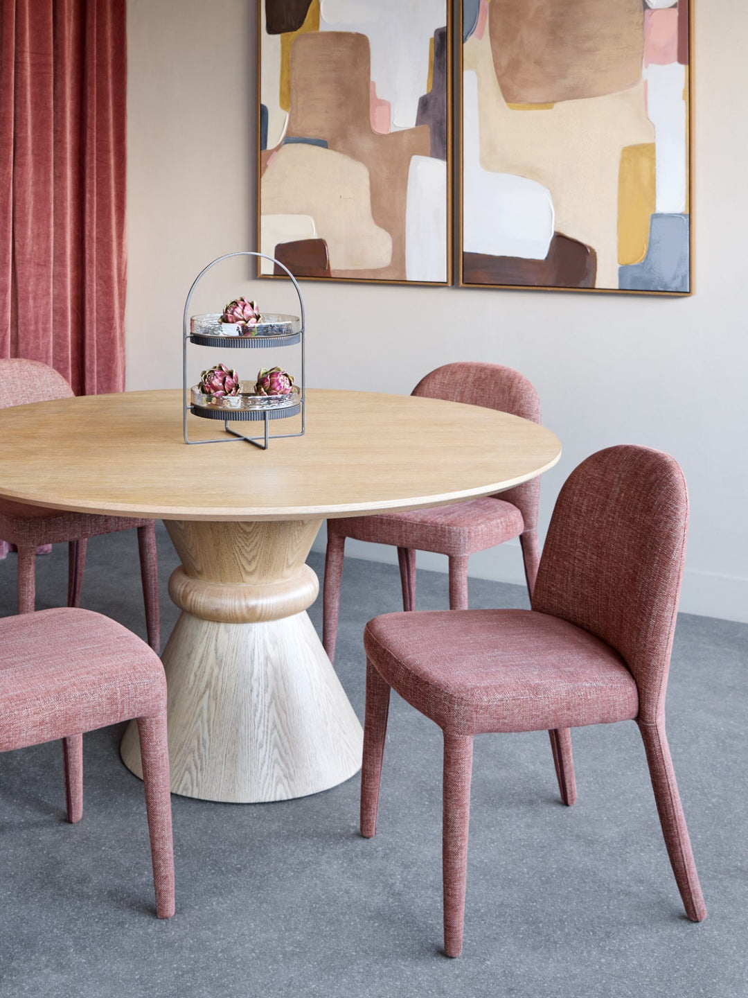 Dining room with a round wooden table and pink chairs, abstract art on the wall.