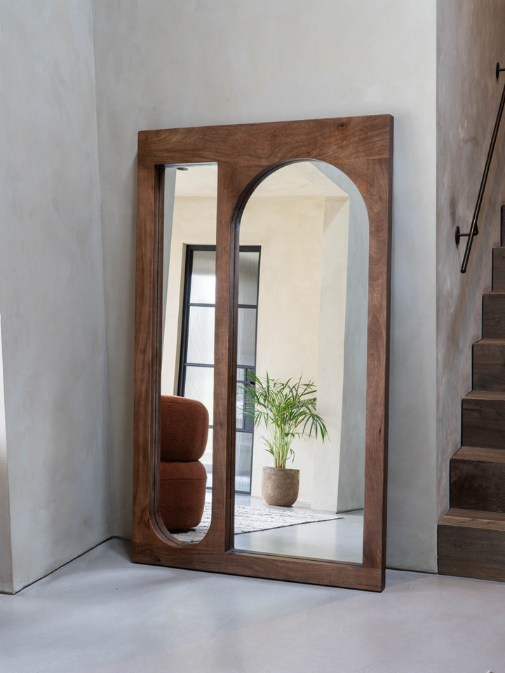Wooden-framed mirror leaning against a wall with a neutral background