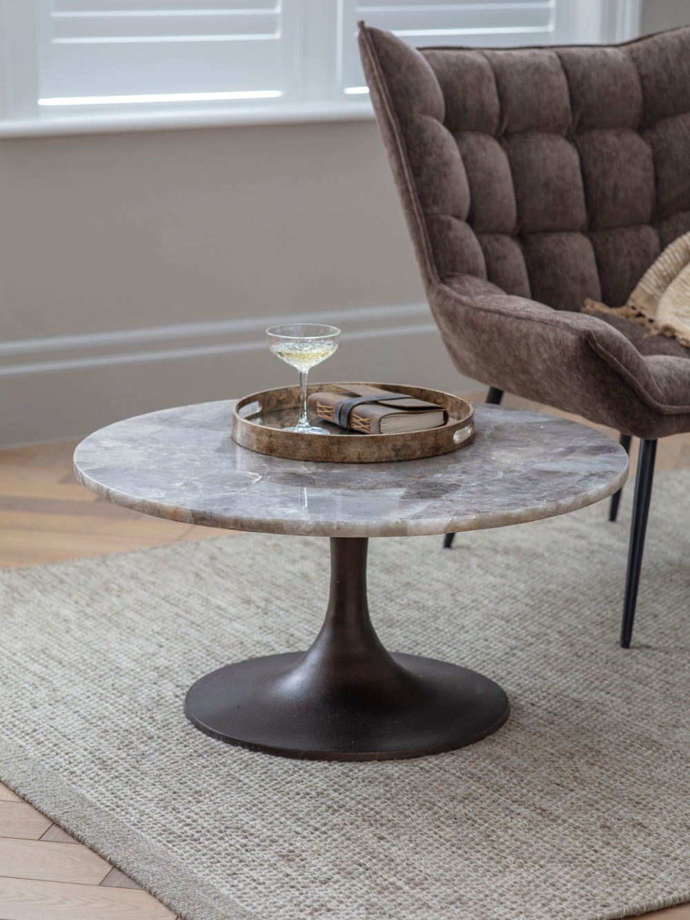 Round marble coffee table with a glass and tray in a room with a chair and rug.