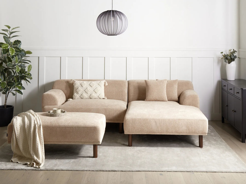 Beige sectional sofa in a modern living room with a plant and side table.