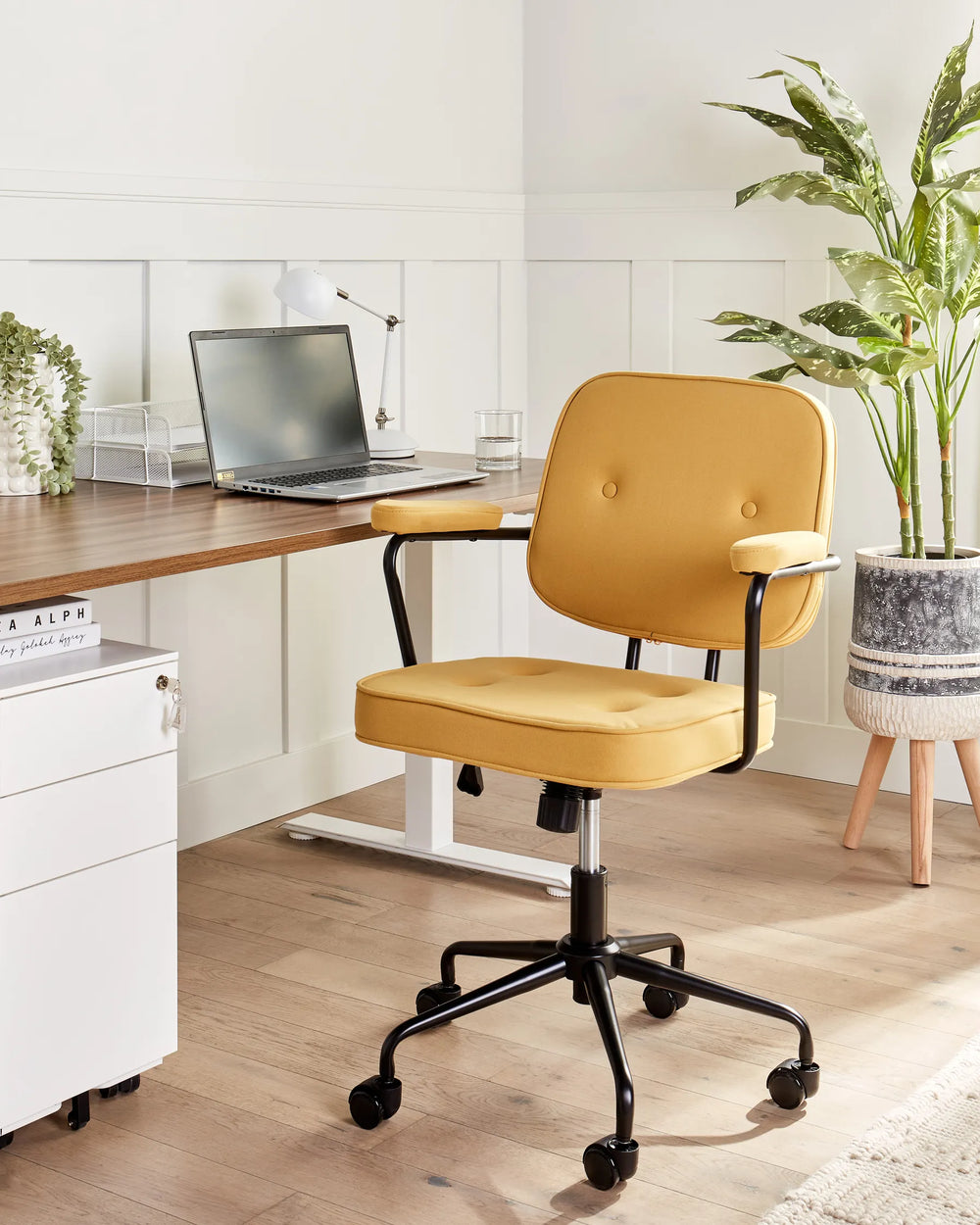 Yellow office chair in front of a desk with a laptop, surrounded by plants and office supplies.