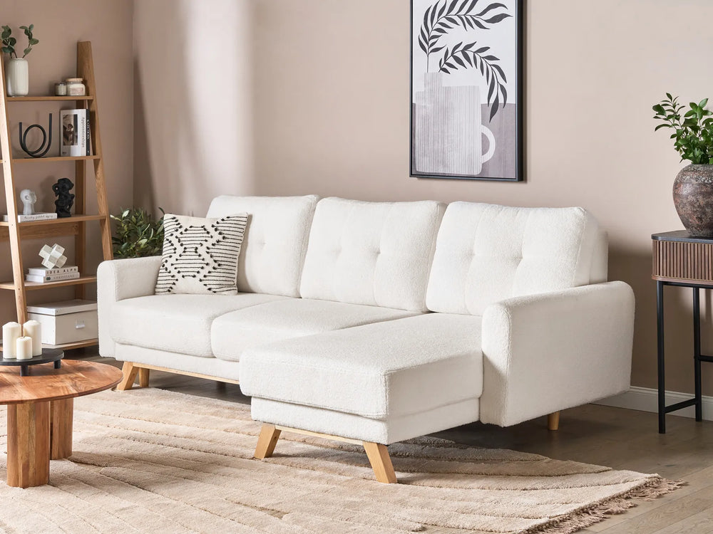 White sectional sofa in a living room with wooden coffee table and shelves.