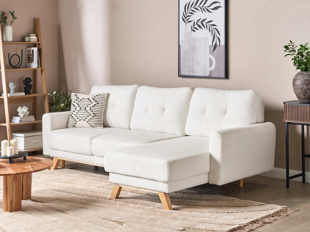 White sectional sofa in a living room with wooden coffee table and shelves.