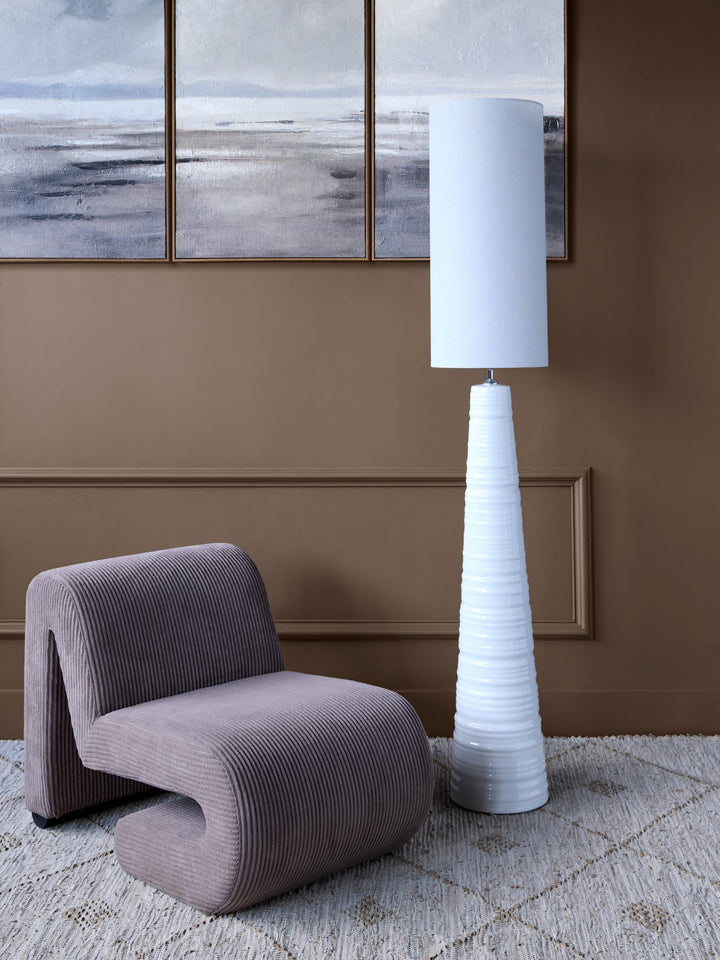 Modern interior with a textured gray chair and a tall white floor lamp against a brown wall with abstract art.