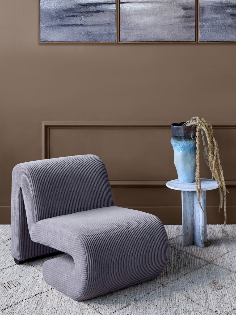 Modern gray chair in a room with abstract art on the wall and a textured rug.