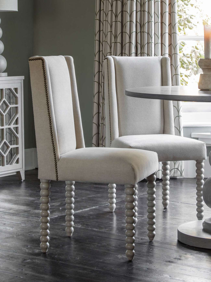 Two upholstered chairs with spindle legs in a dining room setting.