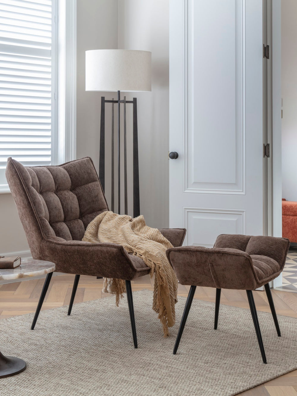 Brown upholstered chairs with a blanket in a room with a lamp and door.