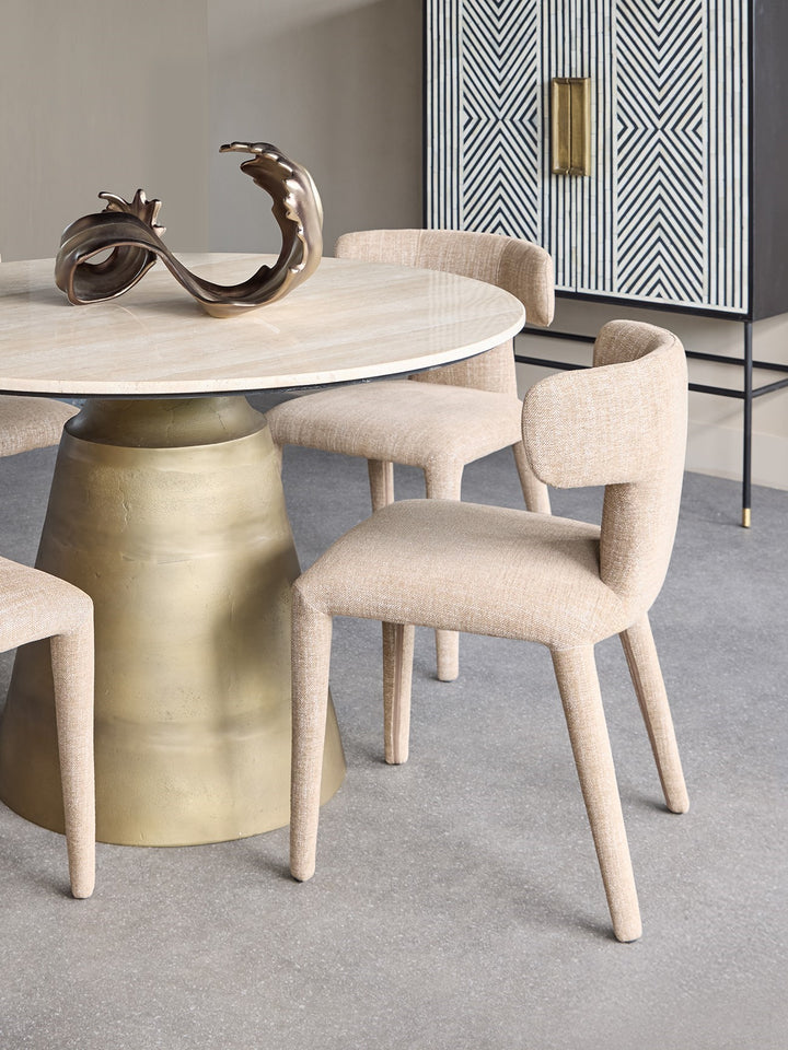 Modern dining table with gold base and marble top, surrounded by beige chairs in a stylish room.